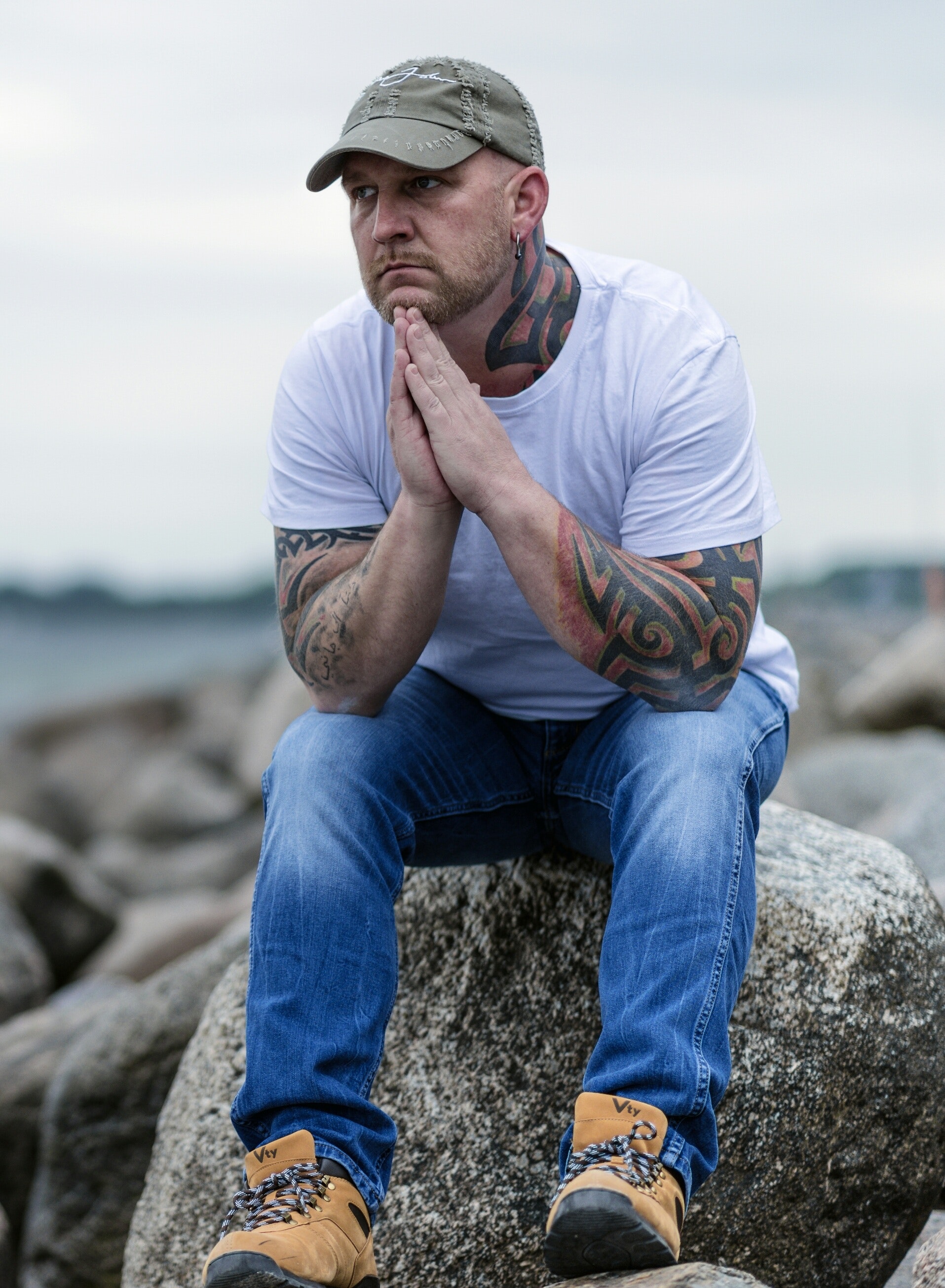 man with tattoos sitting on large rock thinking