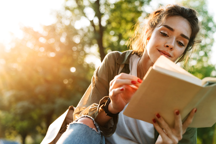 pretty young woman reading book outdoors